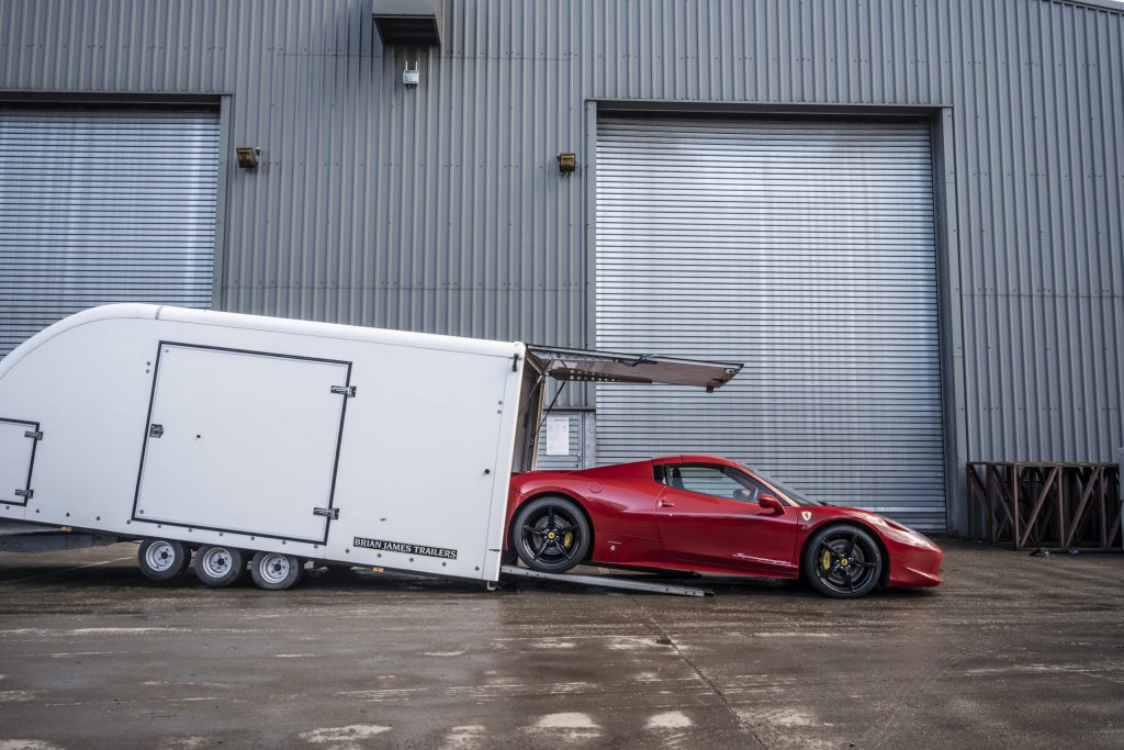 A red Ferrari coming out of a contained delivery trailer